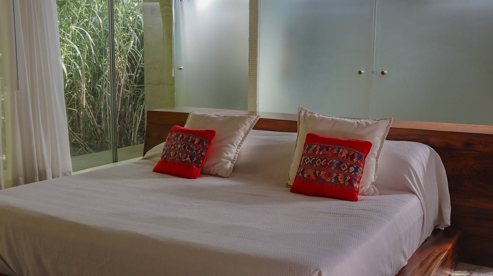 Detalle de cama con cabecera de madera y cojines artesanales